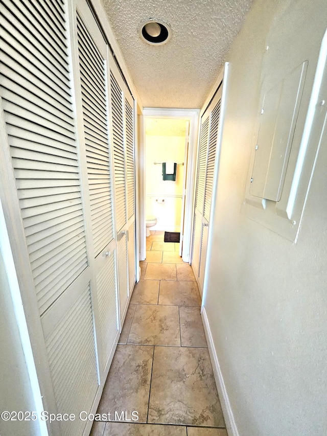 hall with light tile patterned flooring, electric panel, and a textured ceiling