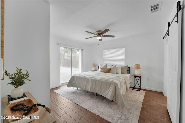 bedroom with access to exterior, hardwood / wood-style floors, a barn door, and ceiling fan