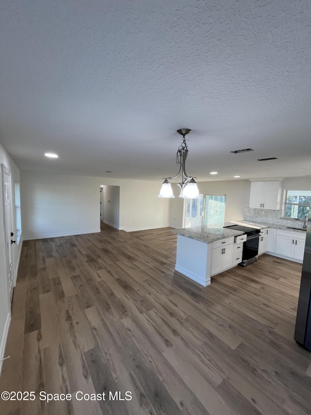 kitchen featuring light stone counters, wood-type flooring, a textured ceiling, hanging light fixtures, and white cabinets