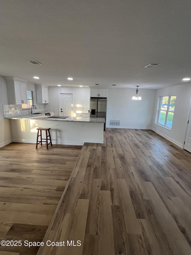 kitchen featuring white cabinetry, light stone counters, a kitchen bar, stainless steel fridge with ice dispenser, and kitchen peninsula