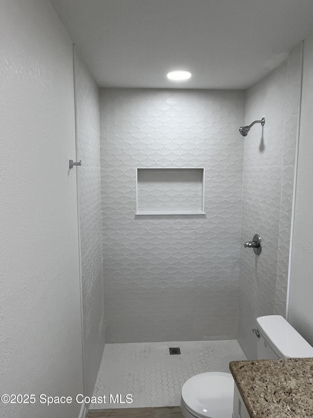 bathroom featuring vanity, toilet, and a tile shower