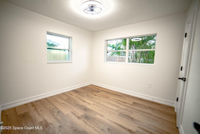 empty room featuring plenty of natural light, light wood-style floors, baseboards, and a textured ceiling