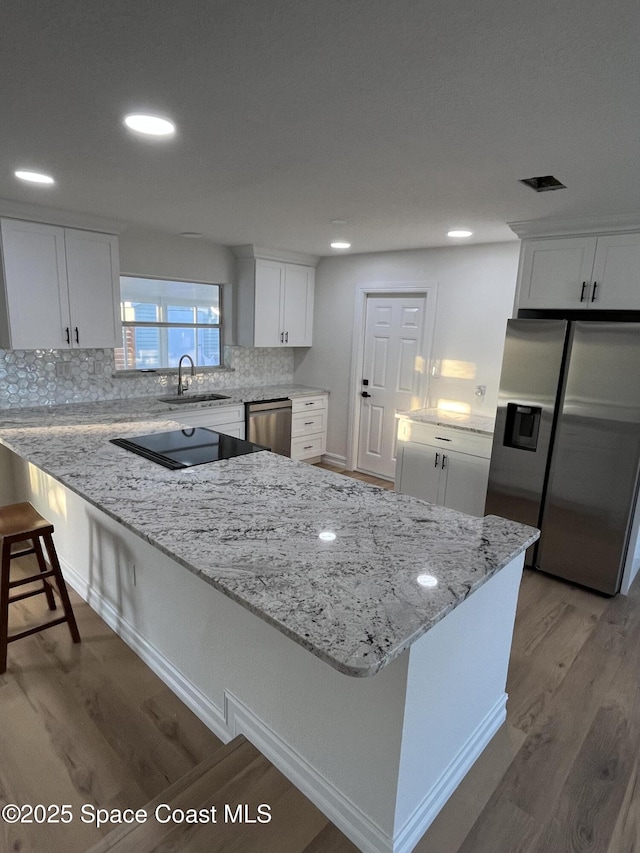 kitchen with light wood-type flooring, appliances with stainless steel finishes, a peninsula, white cabinetry, and a sink