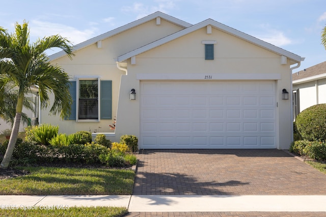 ranch-style house with a garage, stucco siding, and decorative driveway