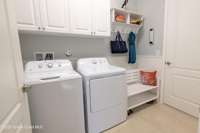 washroom with cabinet space, light tile patterned floors, washing machine and dryer, and wainscoting