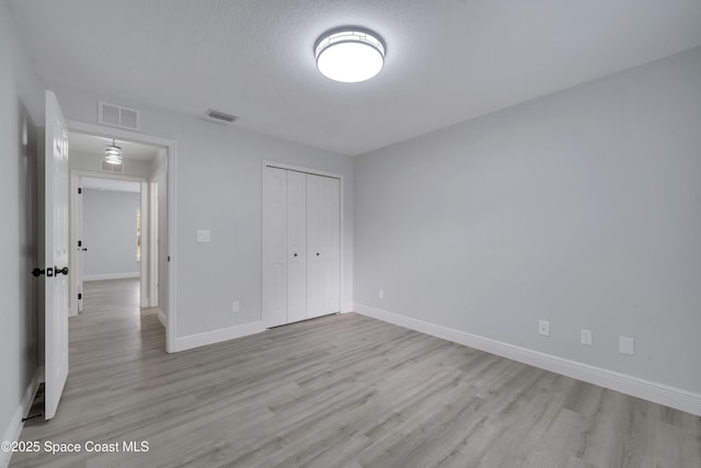 unfurnished bedroom featuring a textured ceiling, light wood-type flooring, and a closet