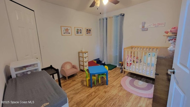 bedroom with wood-type flooring, a nursery area, and ceiling fan