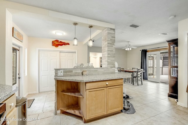 kitchen featuring pendant lighting, a kitchen island, decorative columns, light stone countertops, and light tile patterned flooring