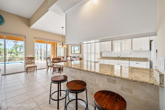 kitchen with pendant lighting, sink, white cabinets, a notable chandelier, and light stone counters