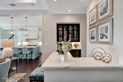 bar with crown molding, a notable chandelier, light stone countertops, dark hardwood / wood-style flooring, and decorative light fixtures