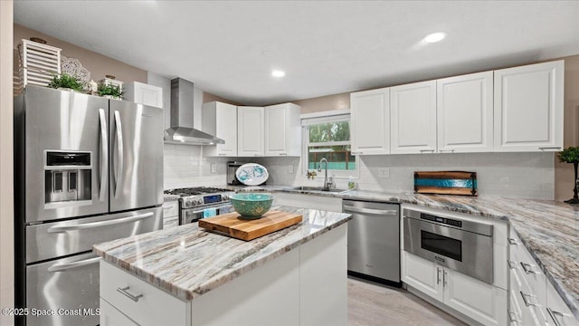 kitchen featuring wall chimney exhaust hood, sink, a center island, appliances with stainless steel finishes, and white cabinets