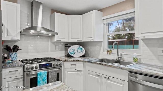 kitchen featuring sink, appliances with stainless steel finishes, wall chimney range hood, light stone countertops, and white cabinets