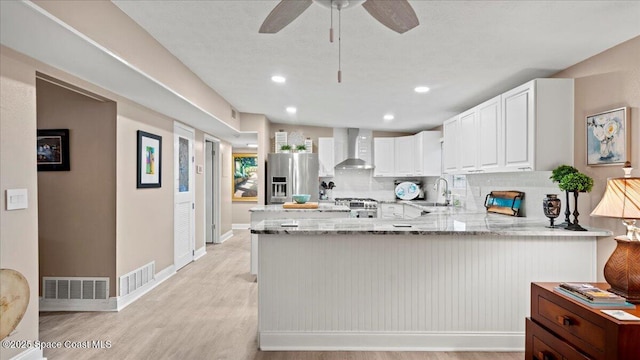 kitchen featuring wall chimney exhaust hood, sink, white cabinetry, kitchen peninsula, and stainless steel appliances