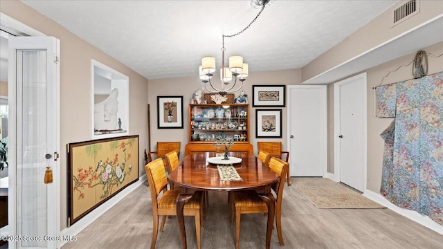 dining area with an inviting chandelier, light hardwood / wood-style floors, and a textured ceiling