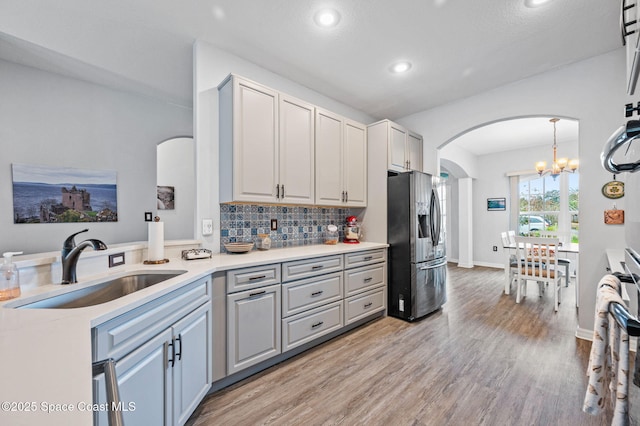 kitchen featuring sink, backsplash, hanging light fixtures, stainless steel fridge with ice dispenser, and light wood-type flooring