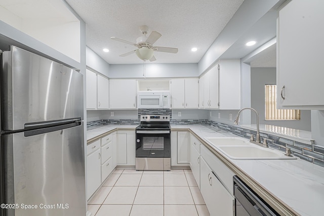 kitchen with sink, a textured ceiling, light tile patterned floors, stainless steel appliances, and white cabinets