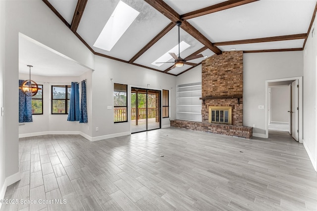 unfurnished living room with built in shelves, a skylight, a brick fireplace, beamed ceiling, and ceiling fan with notable chandelier