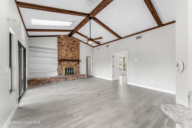 unfurnished living room featuring a brick fireplace, beam ceiling, light hardwood / wood-style floors, and ceiling fan