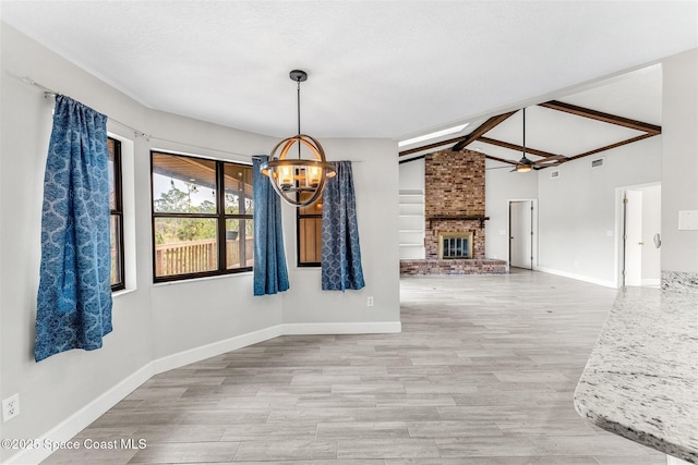 dining space with lofted ceiling with beams, hardwood / wood-style floors, a brick fireplace, and ceiling fan with notable chandelier