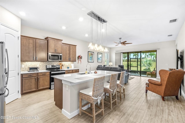 kitchen with pendant lighting, sink, appliances with stainless steel finishes, a kitchen breakfast bar, and an island with sink