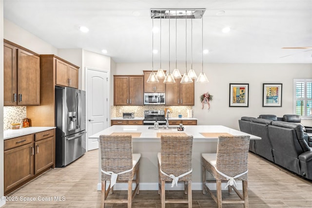 kitchen with pendant lighting, a kitchen breakfast bar, stainless steel appliances, and an island with sink