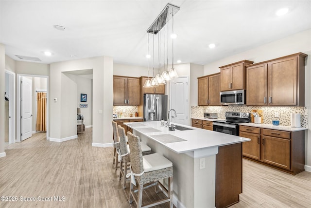 kitchen featuring decorative light fixtures, appliances with stainless steel finishes, a kitchen breakfast bar, an island with sink, and light hardwood / wood-style floors