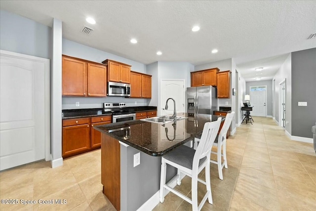 kitchen with appliances with stainless steel finishes, an island with sink, sink, dark stone countertops, and a kitchen bar