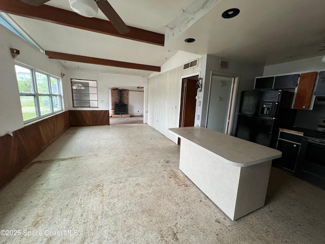 kitchen with vaulted ceiling with beams, black fridge, a wood stove, a kitchen island, and ceiling fan