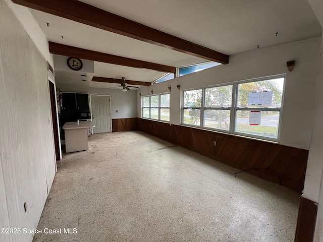 interior space with beamed ceiling, ceiling fan, and wooden walls