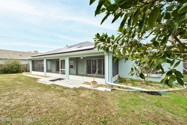 back of house featuring a lawn, a sunroom, and solar panels