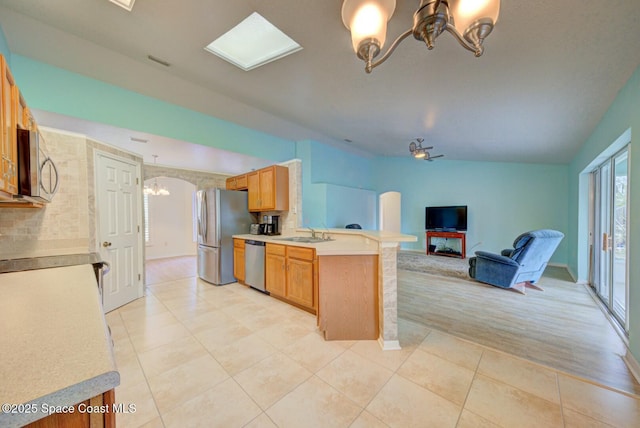 kitchen featuring sink, light tile patterned floors, appliances with stainless steel finishes, kitchen peninsula, and ceiling fan with notable chandelier