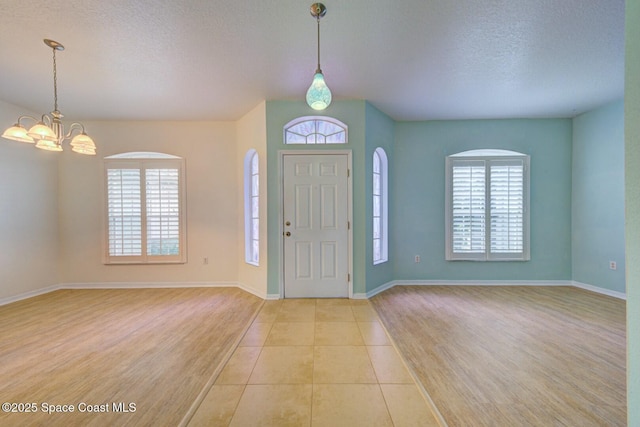 foyer entrance with a chandelier, a textured ceiling, and light tile patterned flooring