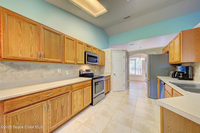 kitchen featuring tasteful backsplash, lofted ceiling, sink, light tile patterned floors, and stainless steel appliances