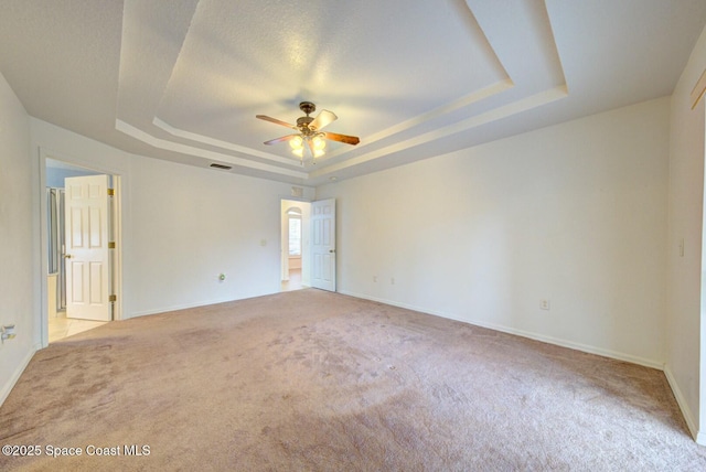 unfurnished room with light carpet, a textured ceiling, ceiling fan, and a tray ceiling