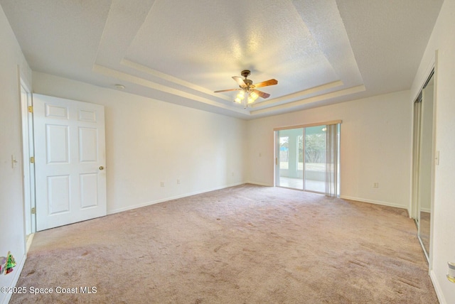 empty room featuring a raised ceiling, ceiling fan, light carpet, and a textured ceiling