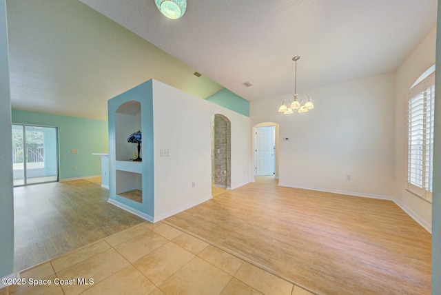 empty room featuring an inviting chandelier, lofted ceiling, light tile patterned floors, and a textured ceiling