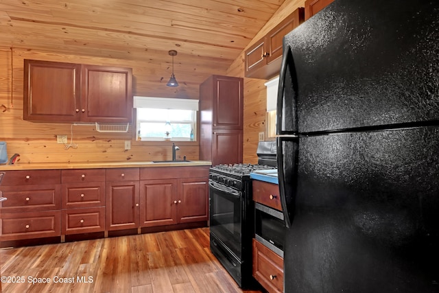 kitchen featuring sink, light hardwood / wood-style flooring, black appliances, decorative light fixtures, and wood walls