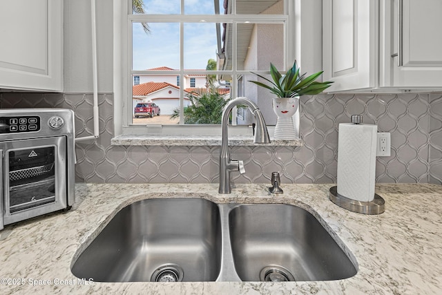 details with tasteful backsplash, sink, light stone counters, and white cabinets