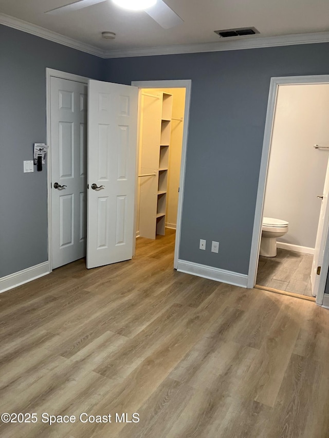 unfurnished bedroom with a walk in closet, connected bathroom, ceiling fan, and light hardwood / wood-style floors