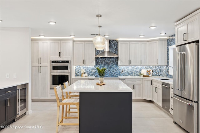 kitchen with sink, appliances with stainless steel finishes, white cabinets, decorative light fixtures, and wall chimney exhaust hood