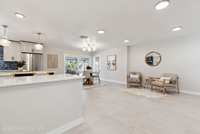 kitchen with light tile patterned floors, backsplash, stainless steel refrigerator, and decorative light fixtures