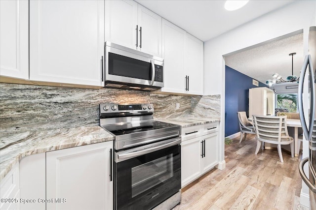 kitchen with light stone counters, light hardwood / wood-style flooring, appliances with stainless steel finishes, decorative backsplash, and white cabinets