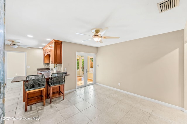 kitchen with light tile patterned floors, ceiling fan, a kitchen breakfast bar, french doors, and kitchen peninsula