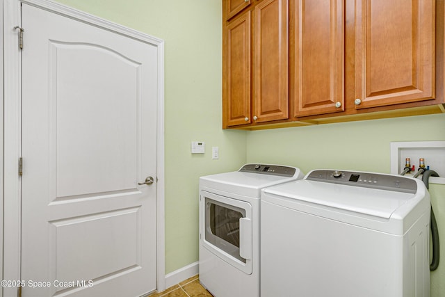 clothes washing area with cabinets, light tile patterned flooring, and washer and clothes dryer