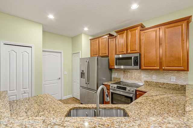 kitchen featuring tasteful backsplash, light stone countertops, appliances with stainless steel finishes, and sink