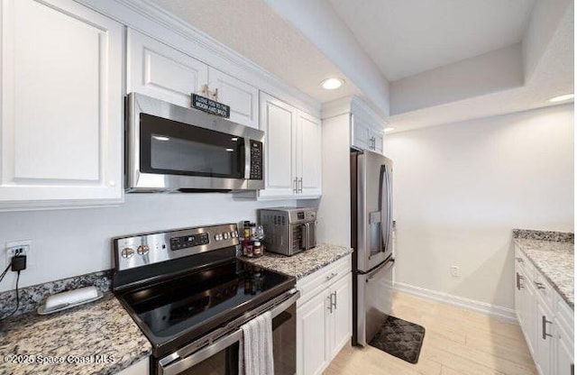 kitchen featuring stainless steel appliances, white cabinets, light stone counters, and light hardwood / wood-style floors