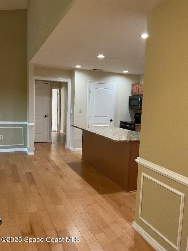 kitchen with light stone counters, black / electric stove, and light wood-type flooring