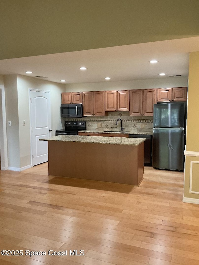 kitchen with light hardwood / wood-style flooring, a center island, light stone countertops, black appliances, and decorative backsplash