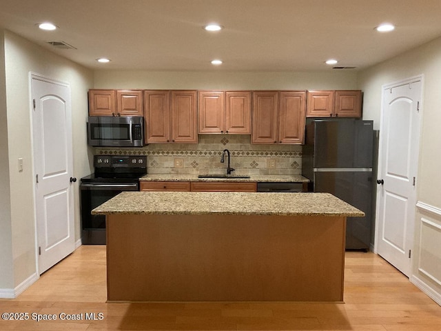 kitchen with sink, backsplash, a center island, light hardwood / wood-style floors, and black appliances