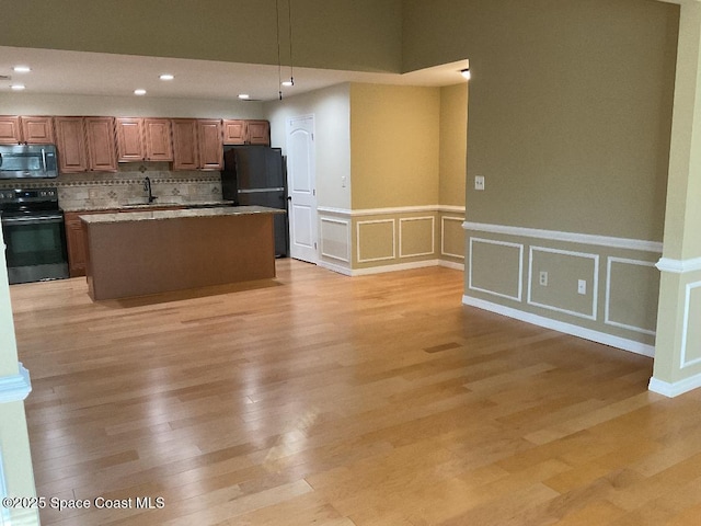 kitchen featuring sink, a center island, hanging light fixtures, light wood-type flooring, and black appliances